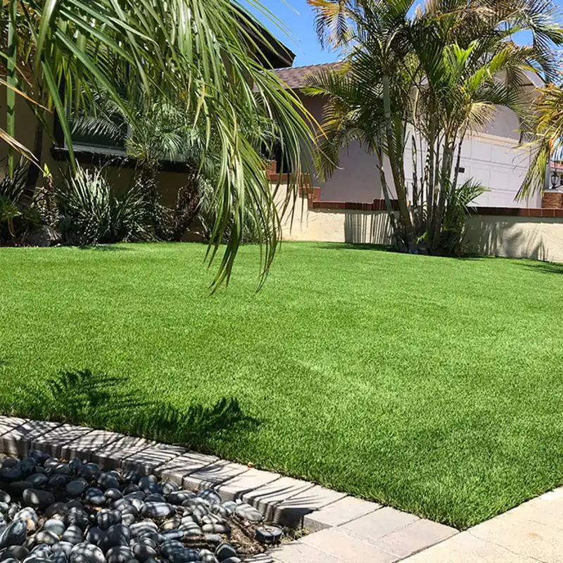 Drought-friendly artificial grass front yard with palm trees and rock border, installed by Scott’s Artificial Grass